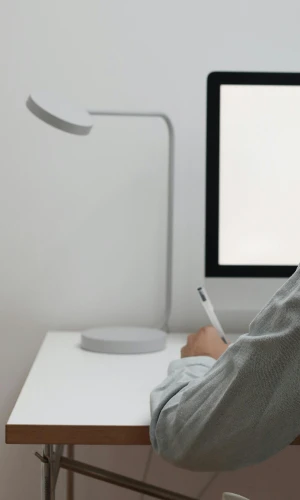 Man writing in an office setting with a blank screen on his computer